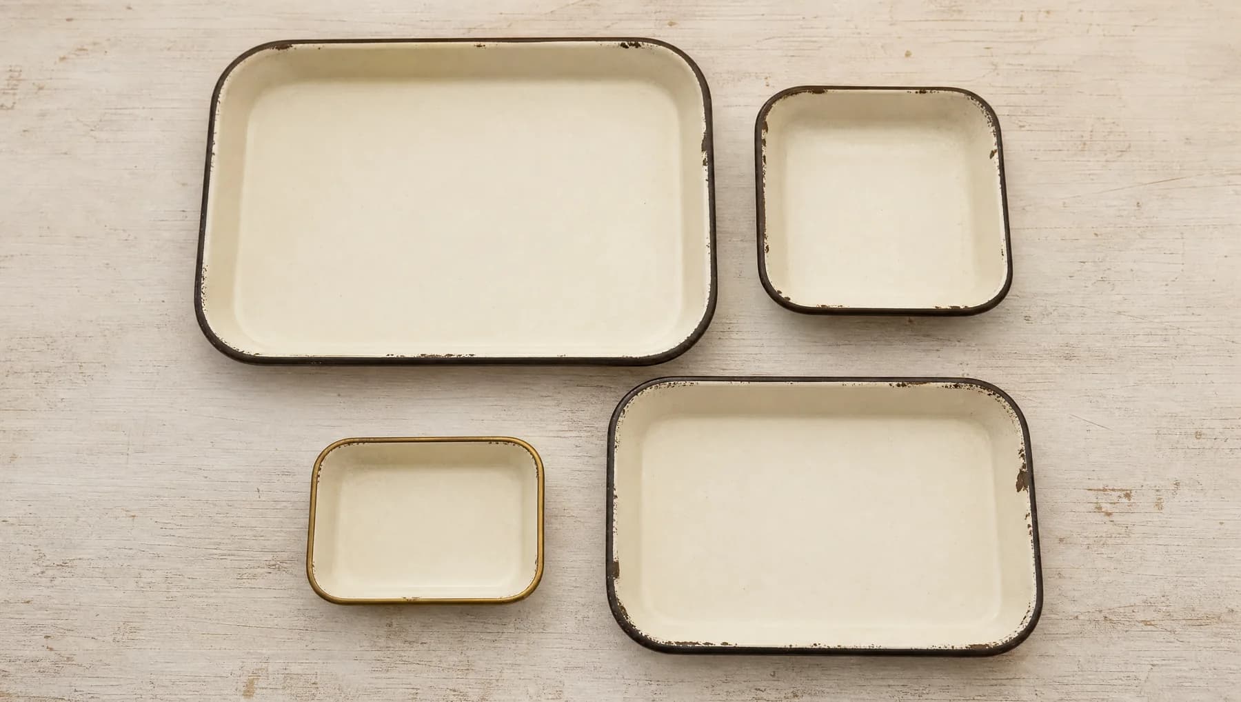 Four empty enamel trays of different sizes on a scrubbed counter